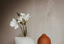 “수면, 바꿔야 할 생활습관의 시작…지금 바로 실천할 수 있는 건강 수면 루틴” a vase with a flower and two bottles of essential oils on a table