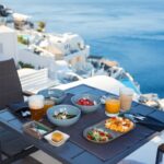 변화하는 여성 건강관리, 작은 습관부터 시작하세요 Breakfast on a balcony overlooking the sea and white buildings.