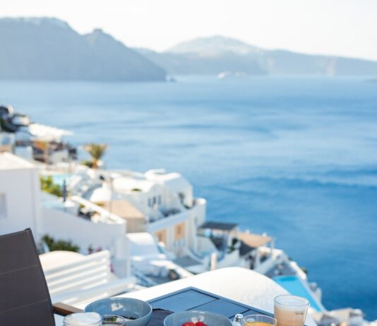 변화하는 여성 건강관리, 작은 습관부터 시작하세요 Breakfast on a balcony overlooking the sea and white buildings.